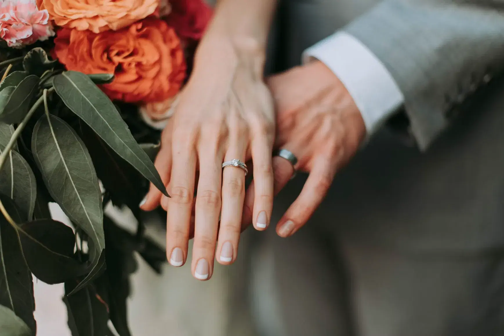 Pareja mostrando sus anillos de matrimonio junto a un ramo de flores